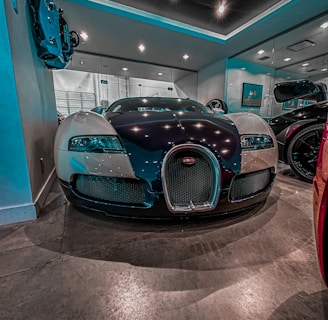 A luxury sports car is parked indoors under a ceiling with recessed lighting. The sleek and reflective surfaces of the car reflect the lights above. The room has mirrors on the walls, enhancing the sense of space and adding to the modern and sophisticated setting.